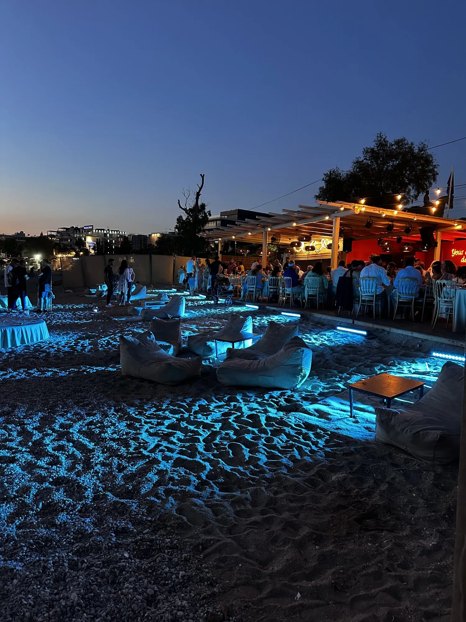 Βραδινό event στην παραλία με μπλε φωτισμό και lounge καθίσματα στην άμμο