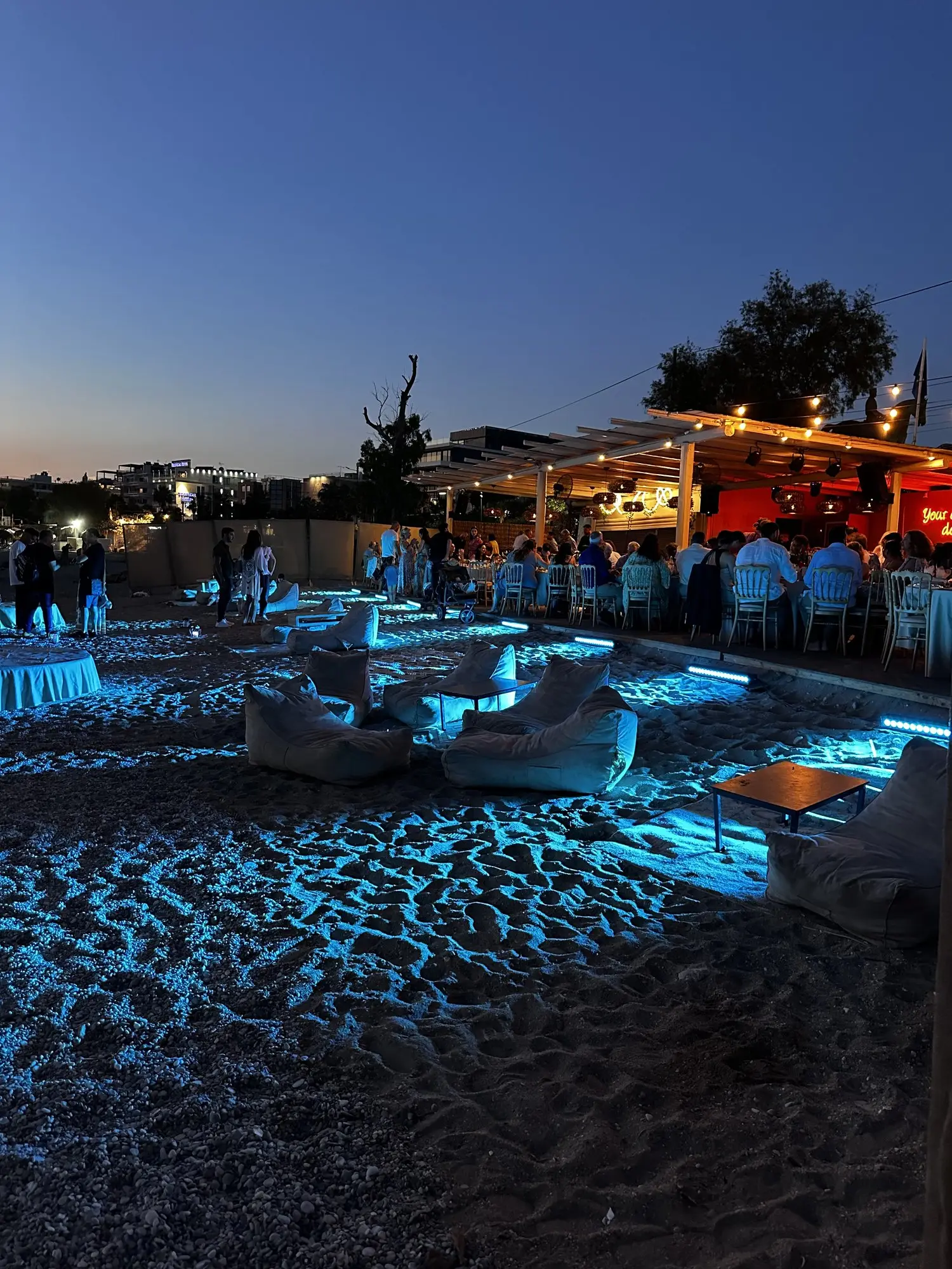 Βραδινό event στην παραλία με μπλε φωτισμό και lounge καθίσματα στην άμμο